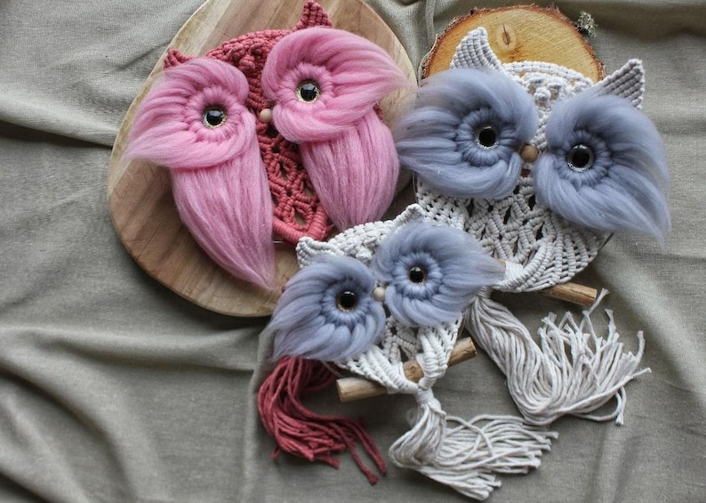 May include: Three handmade macrame owl wall hangings with fringe. The owls are in shades of pink, blue, and white.