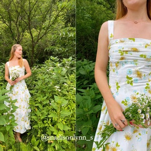 May include: A woman in a white floral dress with a gathered bodice stands in a field of green plants and white flowers. She is holding a bouquet of white flowers in her hand. The text "@madisonlynn_s" is visible in the bottom right corner of the image.