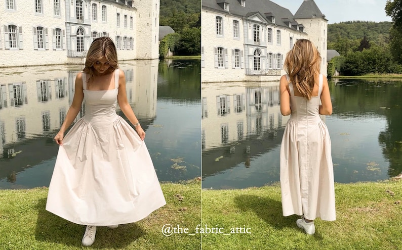 May include: A woman wearing a light beige sleeveless dress with a square neckline and a gathered skirt. She is standing in front of a white building with a pond in the foreground. The text "@the_fabric_attic" is visible in the bottom right corner of the image.