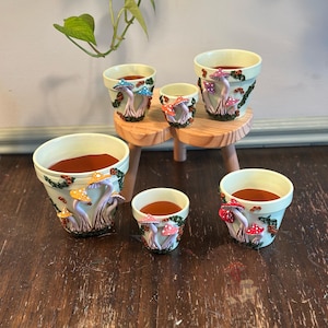 May include: A white ceramic mug with a black handle and the text "But First, Coffee" in a bold, black font. The mug is set against a blurred background, suggesting a cozy setting.