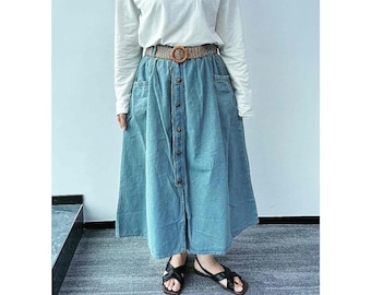 May include: A light blue denim skirt with a button front and a brown woven belt. The skirt has two pockets on the front and falls to the ankles.