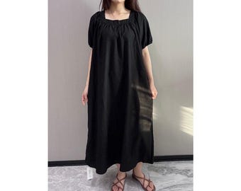 May include: A black midi dress with a square neckline and short, puffed sleeves. The dress has a loose, flowing silhouette and falls to mid-calf. The model is wearing brown sandals.