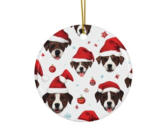 May include: A round, white Christmas ornament featuring a repeating pattern of brown and white dogs wearing red Santa hats. The ornament also includes red and gold Christmas ornaments and snowflakes.