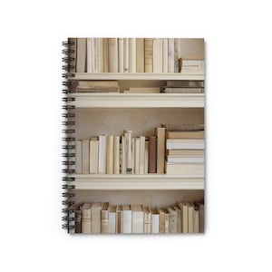 Könnte beinhalten: Spiralgebundenes Notizbuch mit einem Foto eines Bücherregals voller alter Bücher. Die Bücher sind in Creme-, Beige- und Brauntönen gehalten und erzeugen eine warme, neutrale Farbpalette. Das Design des Notizbuchs erinnert an eine klassische, literarische Ästhetik.