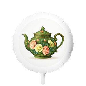 Può includere: Una teiera verde con un design floreale con rose rosa, gialle e pesca. La teiera ha un manico e un beccuccio curvi, su sfondo bianco. L'immagine è su un palloncino bianco.