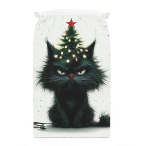 May include: A white drawstring bag featuring a grumpy black cat with a Christmas tree on its head. The cat has a red nose and is surrounded by a Christmas tree with lights and a red star on top. The cat is sitting on a white background.