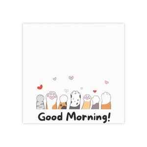 May include: A square white notepad featuring a row of seven colorful cat paws at the bottom, each with distinct fur patterns and colors. Small red and pink hearts are scattered above the paws, and the text Good Morning! is printed in black.
