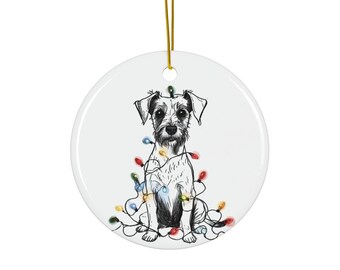 Puede incluir: Adorno navideño redondo de cerámica blanca con una ilustración en blanco y negro de un perro Schnauzer. El perro está sentado y envuelto en luces navideñas de colores. Una cuerda dorada está unida para colgarlo.