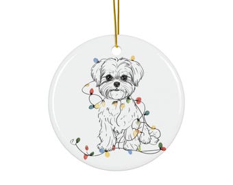 May include: A white ceramic Christmas ornament featuring a line drawing of a fluffy dog tangled in colorful Christmas lights. The ornament has a gold hanging string.