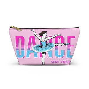 May include: Pink zippered pouch with a ballerina graphic and the word "DANCE" in large letters. The ballerina is wearing a blue tutu and is in a ballet pose. The text "STRUT YOUR STUFF" is below the word "DANCE".