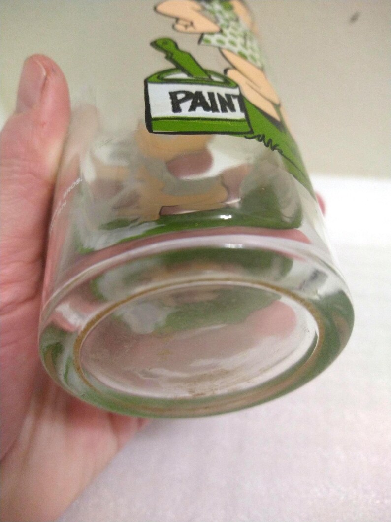 Op de afbeelding: Een helder glazen drinkglas met een cartoonillustratie van een persoon die een verfpot houdt. De verfpot is gelabeld met "PAINT".
