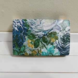 May include: Rectangular decorative object with a floral design. The artwork features a mix of blue, green, and yellow flowers with green leaves. The background is a light color, and the overall style is reminiscent of a watercolor painting.