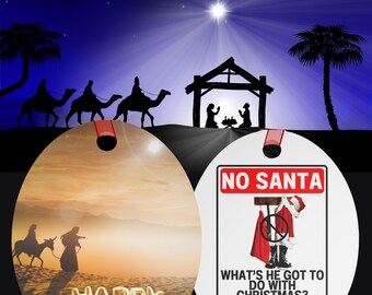 Puede incluir: Un adorno redondo y blanco con una cinta roja. La parte delantera del adorno presenta una escena de puesta de sol con tres reyes magos montando camellos. El texto "HAPPY BIRTHDAY JESUS" está en letras doradas. La parte posterior del adorno presenta un cartel blanco con el texto "NO SANTA" y una imagen de dibujos animados de Santa Claus. El texto "WHAT'S HE GOT TO DO WITH CHRISTMAS? Absolutely nothing." está debajo de la imagen.