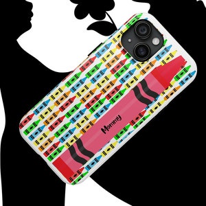 Pode incluir: Uma capa de telefone branca com um padrão de giz de cera colorido e a palavra "Mommy" em um giz de cera rosa. A capa tem um recorte para a lente da câmera.