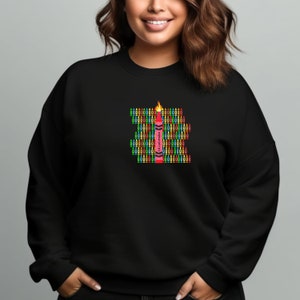 Puede incluir: Una sudadera negra con un gráfico de un crayón rojo. El crayón está rodeado de crayones más pequeños de varios colores. El texto en el crayón dice "Lil' Crayon".