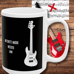 May include: White ceramic mug with a black background and a white outline of a bass guitar. The text "NO SHEET MUSIC NEEDED JIMI" is printed on the mug.
