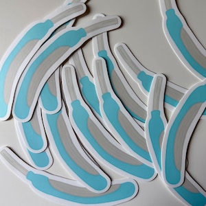 May include: A collection of stickers featuring a curved design with a light blue handle and a gray blade. The stickers have a white border and are scattered across a white surface.