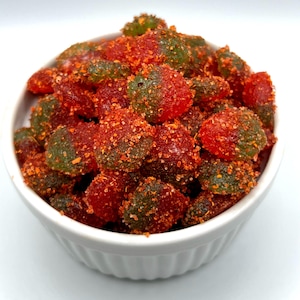 May include: A white bowl filled with red and green gummy candies covered in a red and white sugar coating.