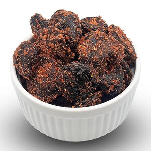 May include: A white bowl filled with dark, dried plums coated in a red, sugary glaze.