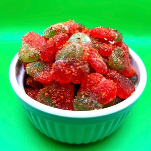 May include: A white bowl filled with red and green gummy candies covered in a red and white powder.