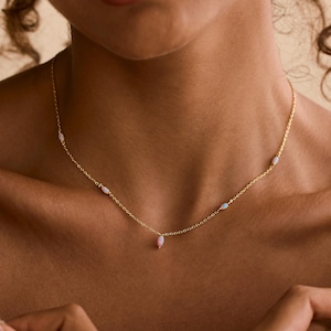 May include: A delicate gold necklace featuring small, light pink teardrop-shaped beads. The necklace is worn around the neck. The words "PEARL ECLIPSE DESIGNS" are printed in white at the bottom of the image.