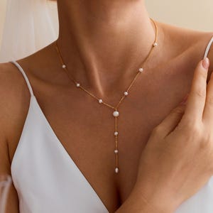 May include: A gold chain necklace featuring a Y-shaped drop design with small, round white pearls spaced along the chain. The necklace includes a central pearl accent where the chain splits into a vertical drop, ending with a single pearl pendant.