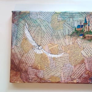May include: A painting on canvas with a collage of old book pages. The painting features a white owl flying towards a blue and white castle with a brown stone bridge. The castle is surrounded by green trees and a blue sky. The painting is signed in the bottom right corner.