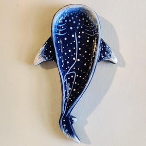 May include: A ceramic whale shark-shaped dish. The dish is dark blue with white polka dots and white accents on the fins and edges. The dish is designed to resemble a whale shark.