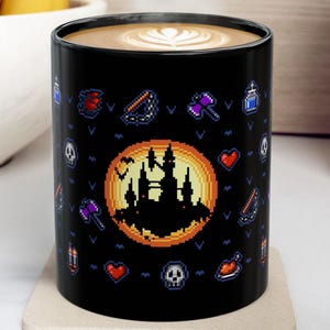 May include: Black ceramic coffee mug with a pixelated design featuring a castle silhouette within an orange circle, surrounded by various pixel art icons. The mug contains a latte with a white design on top.