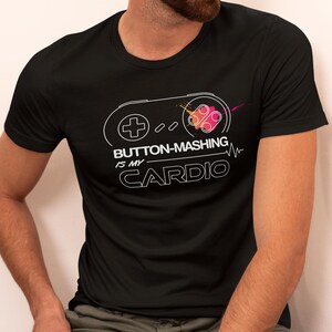 May include: Black t-shirt with a white outline of a video game controller and the text "Button-Mashing is my Cardio" with a pink and orange color splash.