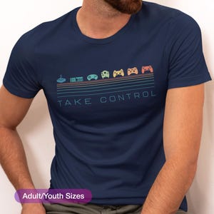 May include: Navy blue t-shirt with a retro video game controller design. The design features a series of colorful controllers and the text "TAKE CONTROL" in a matching font. The shirt is available in adult and youth sizes.