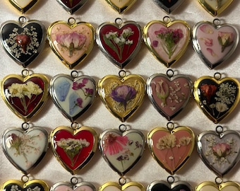 May include: A collection of heart-shaped pendants with dried flowers encased in resin. The pendants have gold, silver, and black metal frames. Each pendant features a unique arrangement of colorful dried flowers.