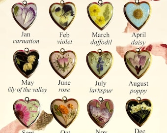 May include: A collection of twelve heart-shaped pendants, each containing a pressed flower and labeled with a month and flower name. The pendants have gold-colored frames and are arranged in a grid. The flowers include carnation, violet, daffodil, daisy, lily of the valley, rose, larkspur, poppy, aster, marigold, chrysanthemum, and narcissus.