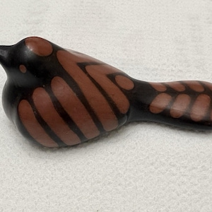 Puede incluir: Figura de pájaro de cerámica con cabeza y cola negras, y cuerpo marrón con un patrón de rayas. El pájaro tiene un cuerpo redondeado y un pico puntiagudo. La figura está sobre una superficie blanca.