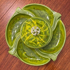 以下が含まれることがあります： 中央に蓋付きのボウルと4つのセクションがある、ヴィンテージの緑色のセラミック製サービングディッシュ。 ディッシュは、黄色と緑色の渦巻き模様の光沢仕上げです。 銀色の装飾要素が蓋を飾っています。