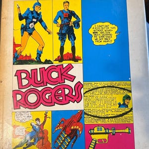 Può includere: Una copertina di fumetto vintage per "The Collected Works of Buck Rogers nel 25° secolo". La copertina presenta vignette di fumetti con personaggi in tute spaziali blu, il titolo "BUCK ROGERS" in grandi lettere rosa e fumetti.