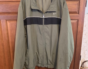 May include: Olive green Nike track jacket with a black stripe across the chest. The jacket has a white stripe above the black stripe and a small white Nike logo on the chest. It features a full zipper and a collared neckline.
