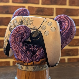 Könnte beinhalten: Ein weiß-schwarzer Videospiel-Controller mit lila dekorativen Akzenten, der auf einem holzfassförmigen Ständer ruht. Der Controller hat ein Wellenmuster-Design, vor einem Hintergrund aus Backsteinmauerwerk.