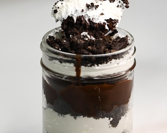 May include: A glass jar filled with layers of chocolate pudding, whipped cream, and crushed Oreo cookies. A spoon is holding a bite of the dessert.
