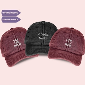Può includere: Tre cappellini da baseball bordeaux e neri. I cappellini bordeaux hanno un testo ricamato bianco che recita "EAT THE RICH" e "FCK NZS". Il cappellino nero ha il testo "o bella ciao". I cappellini sono usurati.
