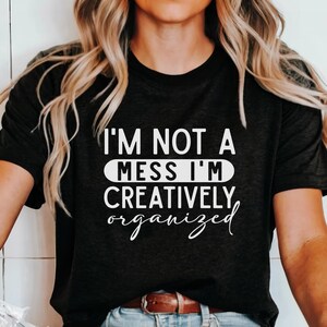 May include: A black t-shirt with white text that reads "I'm not a mess I'm creatively organized".