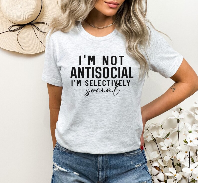 Op de afbeelding: Een grijs T-shirt met de tekst "I'm not antisocial I'm selectively social" in zwart gedrukt.