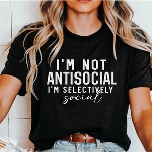 Op de afbeelding: Een zwart T-shirt met witte tekst die "Ik ben niet antisociaal, ik ben selectief in mijn sociale leven" zegt.