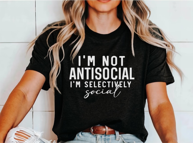 Op de afbeelding: Een zwart T-shirt met witte tekst die "Ik ben niet antisociaal, ik ben selectief in mijn sociale leven" zegt.