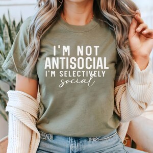 Op de afbeelding: Een groen T-shirt met de tekst "I'm not antisocial I'm selectively social" in wit.