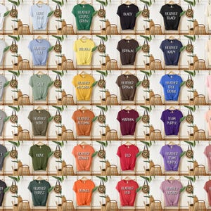以下が含まれることがあります： さまざまな色のTシャツのコレクションで、それぞれ木製のハンガーに展示されています。シャツは、白、青、緑、黒、黄色、茶色、ネイビー、ピンクなど、さまざまな色があります。各シャツには異なるテキストが印刷されています。