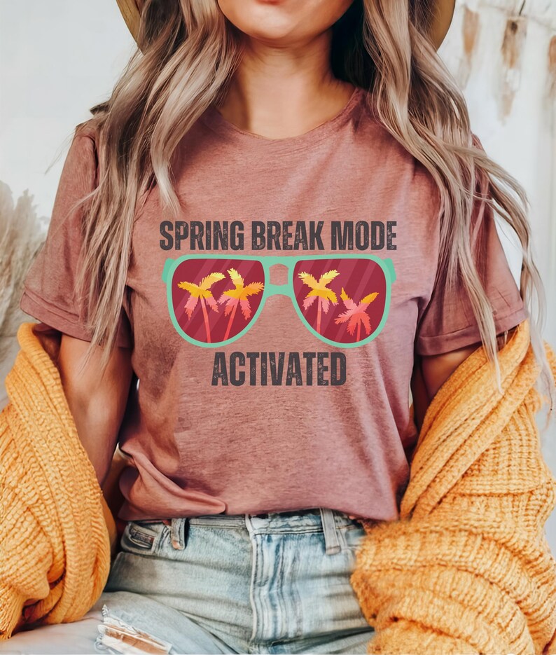 以下が含まれることがあります： 「SPRING BREAK MODE ACTIVATED」の文字が入ったモーヴ色のTシャツ。ヤシの木が入ったサングラスのグラフィック。青いジーンズと黄色のセーターを着ている人。
