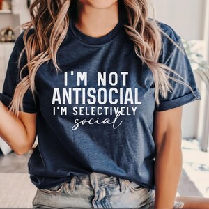 Op de afbeelding: Een marineblauw T-shirt met witte tekst die "Ik ben niet antisociaal, ik ben selectief sociaal" zegt.