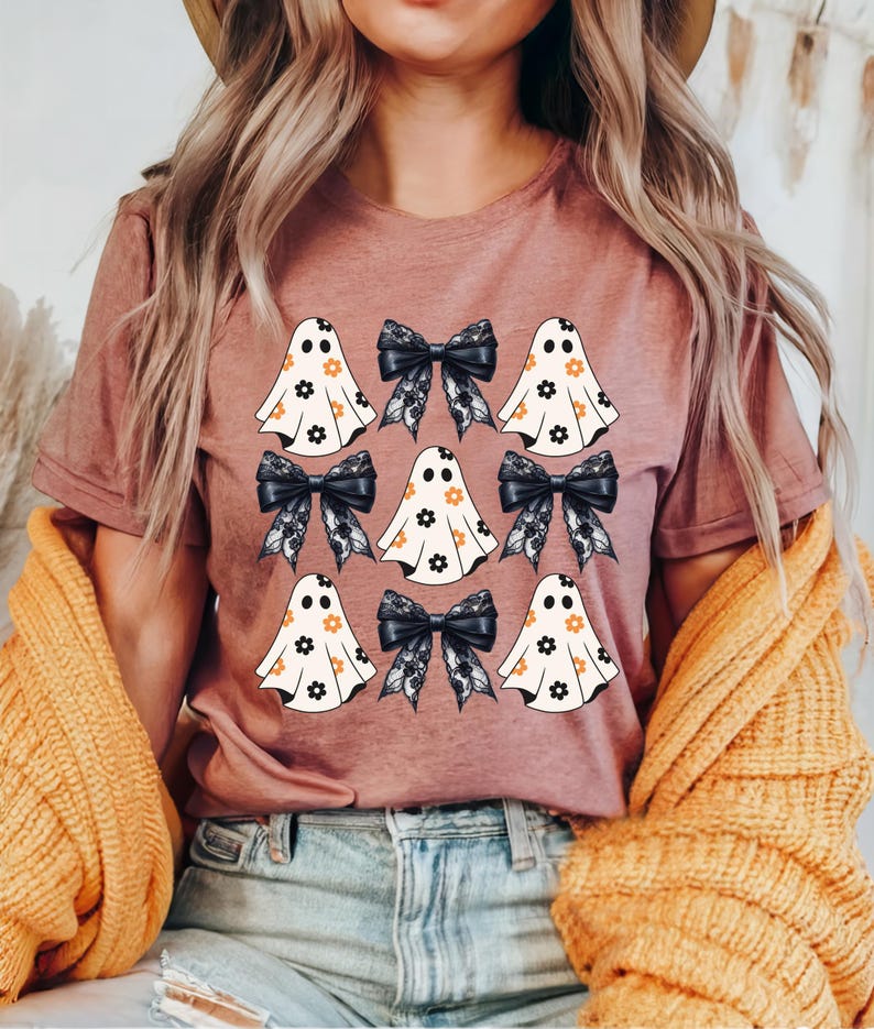 Puede incluir: Una camiseta malva con un estampado gr&aacute;fico de fantasmas con patrones florales y lazos negros.