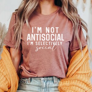 Op de afbeelding: Een mauve t-shirt met de tekst "I'm not antisocial I'm selectively social" in witte letters.